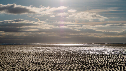 Obraz premium The coastline at low tide with patterns in the sand. An ocean beach with wet sand in the sunlight