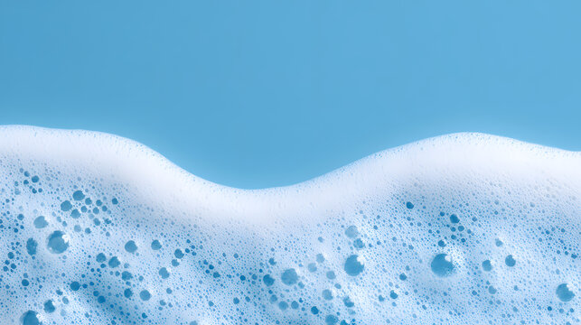 White soap foam or detergent suds with various bubble sizes forming a wavy pattern against a clean solid blue background, ideal for hygiene, cleaning, and laundry concept designs.