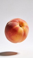 A single ripe peach with vibrant red and yellow hues floats against a clean white background
