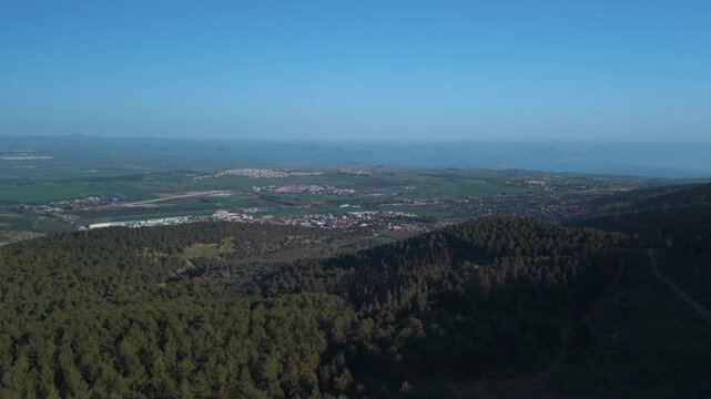 Hatzor HaGlilit and Rosh Pinna towns viewed from a drone above Biriya Forest with Golan Heights in Israel.