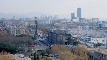 Obraz premium Barcelona cityscape with the columbus monument, bustling avenue and waterfront port vell marina filled with boats, historic buildings and hazy skyline by the sea