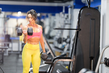 Woman training biceps lifting dumbbells in modern gym