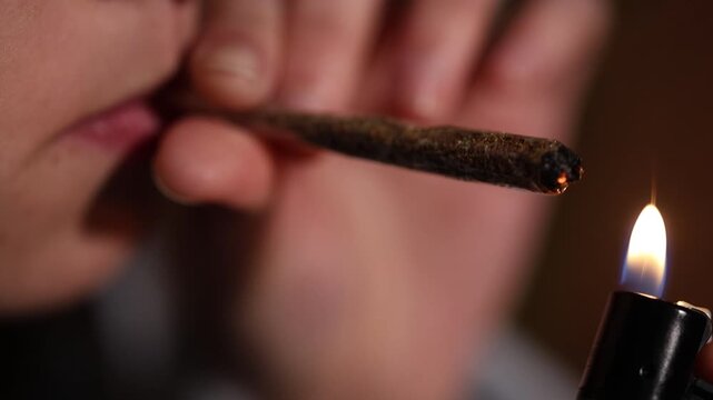 Close-up view of a person lighting a handmade cannabis joint with a lighter and then smoking it