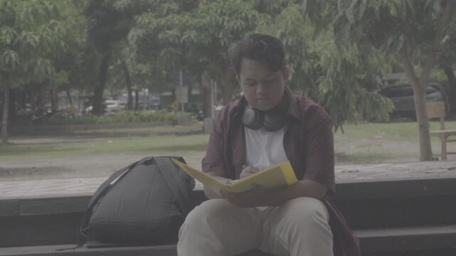 A Southeast Asian student studies in the campus yard alone with books and a tablet. S-Log3, S-Gamut3.Cine
