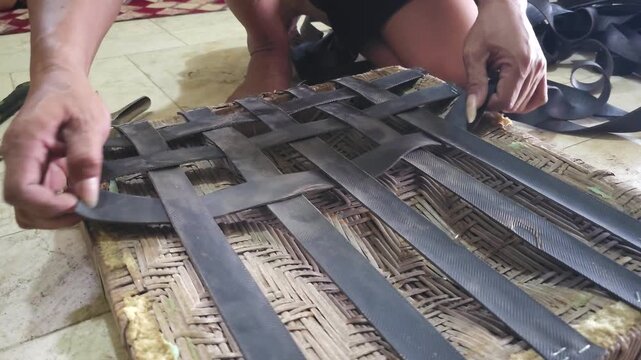 Close up hands weaving black rubber strips onto bamboo chair frame using staple gun for furniture repair