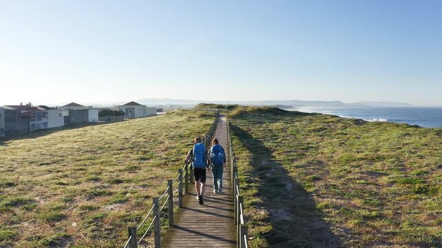 Middle-aged couple with backpacks walking together in Portugal on Camino Portuguese pilgrimage route to Santiago de Compostela. Active lifestyle, travel, and happiness concept during coastal trekking