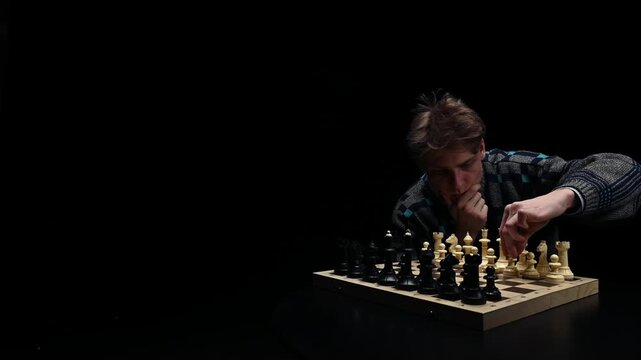 A young man is sitting in front of a chessboard with pieces and thinking about the next move. The chess player is assessing the risks before making the first move. A thoughtful chess player