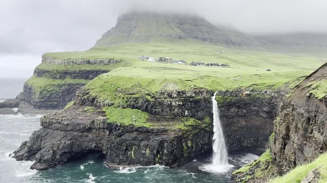 Green landscapes of the Faroe Islands. Incredible view of Mulafossur waterfall flowing into the Atlantic Ocean. Gasadalur village, Vagar Island.