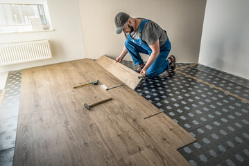 Professional carpenter master worker in blue overalls is joining vinyl or laminate floor covering, home renovation