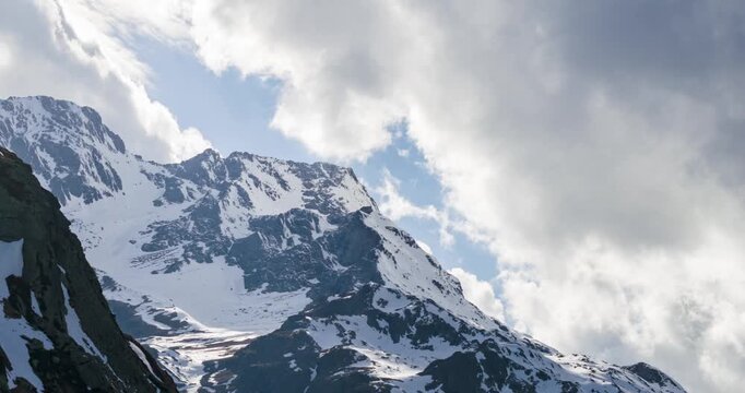 Snow capped mountains reaching towards a blue sky with dramatic white clouds. aerial, timelapse