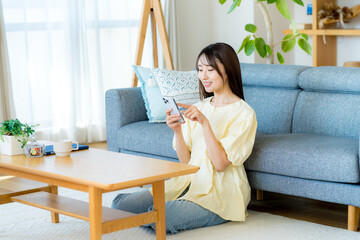 部屋でスマホを操作する女性 © wheeljack