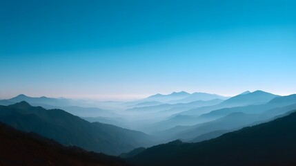 Fototapeta premium Expansive mountain ranges create layered silhouettes against a clear vast blue sky during dawn