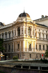 Fototapeta premium A grand horizontal panorama of a majestic Neo-Gothic administrative building featuring a soaring central spire and perfectly symmetrical architecture. The ornate facade is richly decorated with multip
