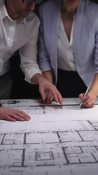 Architects and engineers collaborating on a building blueprint, measuring and discussing plans for a new construction project. Concept of architecture and business in low key lighting