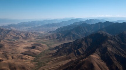 Vast rugged mountain ranges stretch towards the horizon under a clear blue sky showcasing dramatic shadows and geological formations