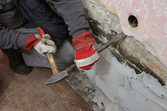 Construction worker demolishing hole at brick wall and mortar with chisel tool and hammer