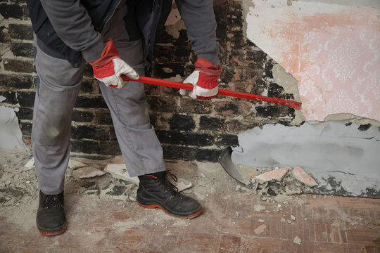 Worker demolishing old building wall using crowbar tool