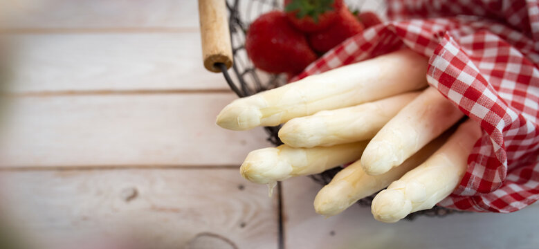 Bundle of seasonal white asparagus in a basket with fresh strawberries. Horizontal background for seasonal gastronomy and healthy nutrition. Close-up.