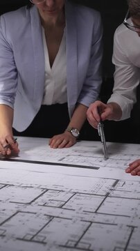 Architects and engineers collaborating on a building blueprint, measuring and discussing plans for a new construction project. Concept of architecture and business in low key lighting