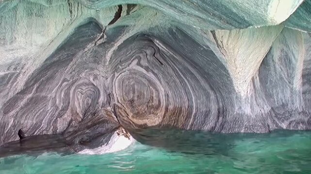 Witness the breathtaking Marble Caves in Patagonia. Serene turquoise waters gently caress ancient, swirling marble walls, revealing nature's intricate geological art. A stunning visual exploration.