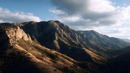 Majestic mountain range bathed in golden hour light with dramatic shadows and rugged terrain