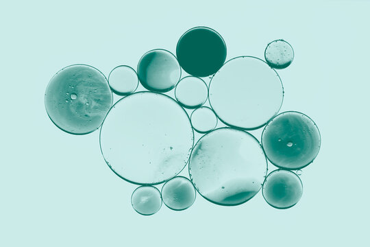 Isolated bubbles and oil droplets against a pastel blue-green background. Macro photograph of an emulsion in water. Droplets of a serum.