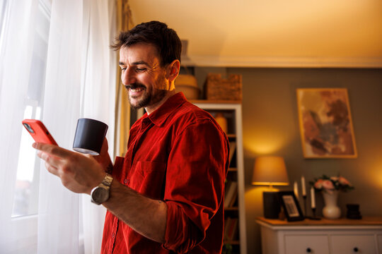 Man drinking coffee and using smart phone while relaxing at home