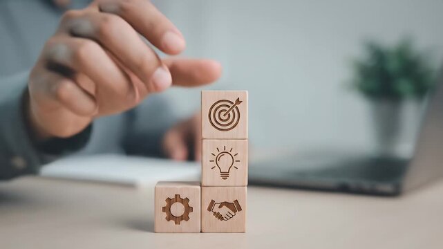 Close-up of a hand placing a wooden block with a target icon on top of stacked cubes displaying business symbols, subtle alignment motion with slow cinematic push-in, soft neutral lighting and shallow