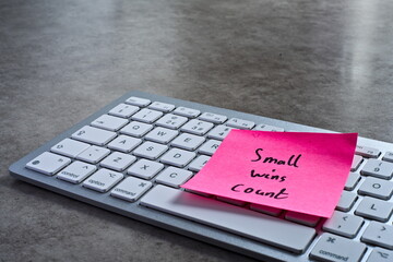 "Small wins count" sticky note left on keyboard. The bright note stands out against the keys, symbolising motivation, productivity, and a focused mindset. © Shannon Muranyi