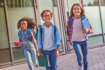 Obraz premium Group of diverse multiethnic kids children elementary middle school kids classmates pupils friends boys and girls rushing out from school running out outside at the end of the lessons