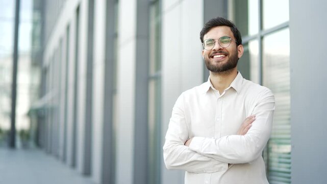 Portrait of happy businessman in a shirt standing on city street near office building. Smiling bearded handsome male worker with crossed arms looking at camera. Template for advertising. Copy space