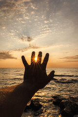 Silhouette hand holding sun over sea horizon at sunset with dramatic sky background