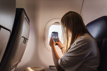 Young woman photographing airplane wing through cabin window during flight © StockMediaSeller