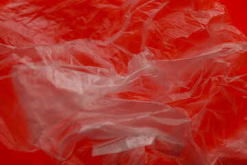 Fototapeta premium Abstract composition of crumpled translucent plastic film on a rich red background creating a dynamic interplay of light and shadow. Numerous folds and creases of the material form a complex visual st