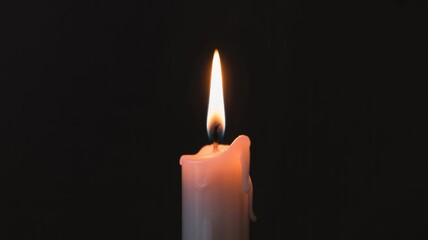 A single lit white candle glows warmly against a dark, dramatic black background.