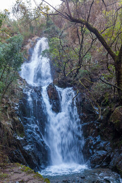A cascading waterfall of Candal (Portugal) flows down dark, wet rocks in a forest
