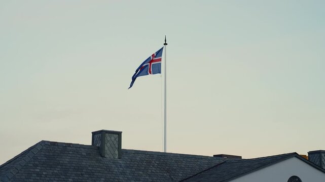Icelandic flag waving on a rooftop against a clear blue sky during sunrise.