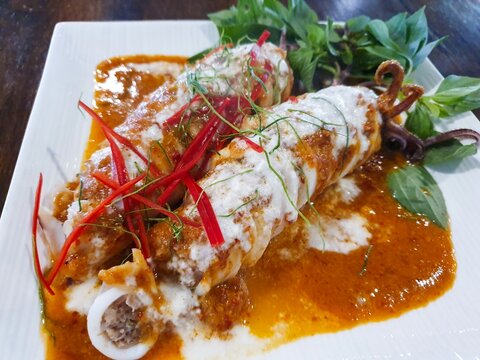 Authentic Thai Chuchi Squid Curry Stuffed with Minced Pork Topped with Thick Coconut Milk Cream and Sliced Kaffir Lime Leaves on White Plate