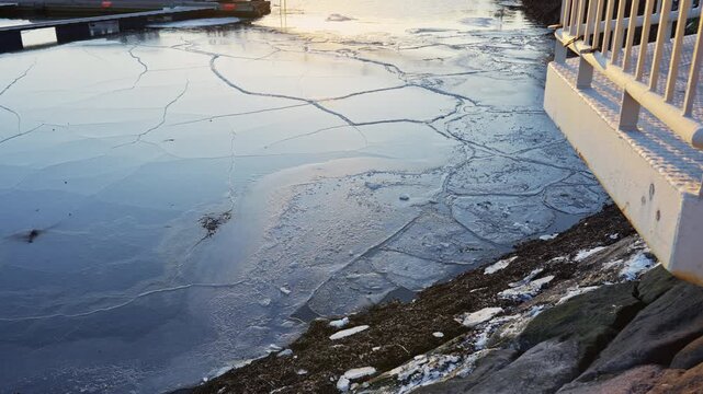 Cracked ice floating on sea water in a harbor with gentle movement under sunrise light.