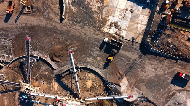 Industrial loader filling dump truck with stone at quarry. Aerial view of a front end loader loading a white truck in an industrial mining area.