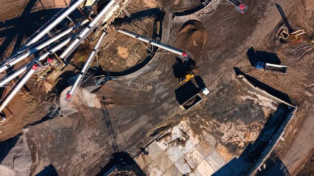 High angle shot of logistics and machinery at stone quarry. View of trucks and a loader operating on the dusty ground of an industrial mining site.