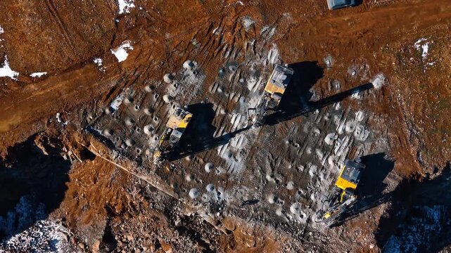 Top down view of drill rigs on quarry bench. Three yellow hydraulic crawler drills boring holes into rock surface for blasting at a granite mine.