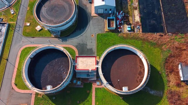 Symmetrical top view of secondary clarification tanks. Close up aerial perspective of circular water treatment tanks with dark liquid and technical walkways.