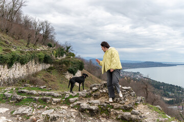 Woman stepping on stone ruins near black dog overlooking New Athos coastline and Black Sea from...