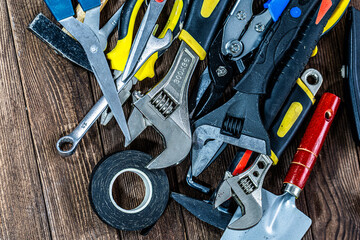 High-resolution image of a complete set of household construction and repair tools arranged on a wooden background. Includes pliers, bolts, hammer, scissors, electrical tape and essential hand tools.