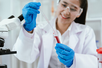 Female scientist wearing safety goggles examining blood samples in test tubes at a laboratory,...