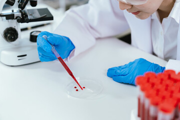 Female scientist wearing safety goggles examining blood samples in test tubes at a laboratory,...
