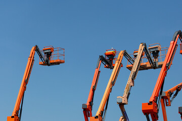 A group of orange and white cranes are in the sky. Mobile construction crane for rent and sale. Aerial work platforms of a cherry pickers with sky background. Boom lifting machine. © Rattanachat