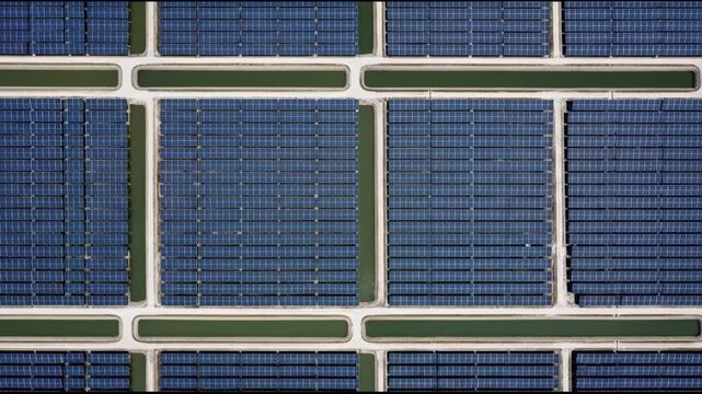 Top-down aerial view of a large solar panel farm arranged in geometric patterns, with water channels.