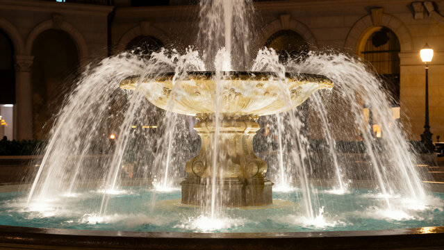 Elegant Ornate Fountain Spraying Water at Night in a Grand Public Square with Classical Architecture and Warm Ambient Lighting